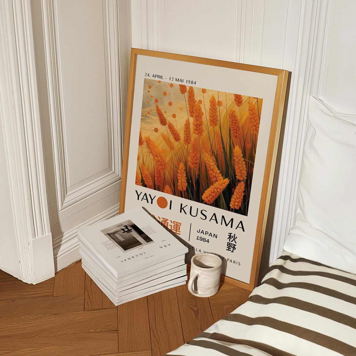 Print leaning on wooden floor showing autumnal wall art of orange wheat plants next to a stack of books and a mug