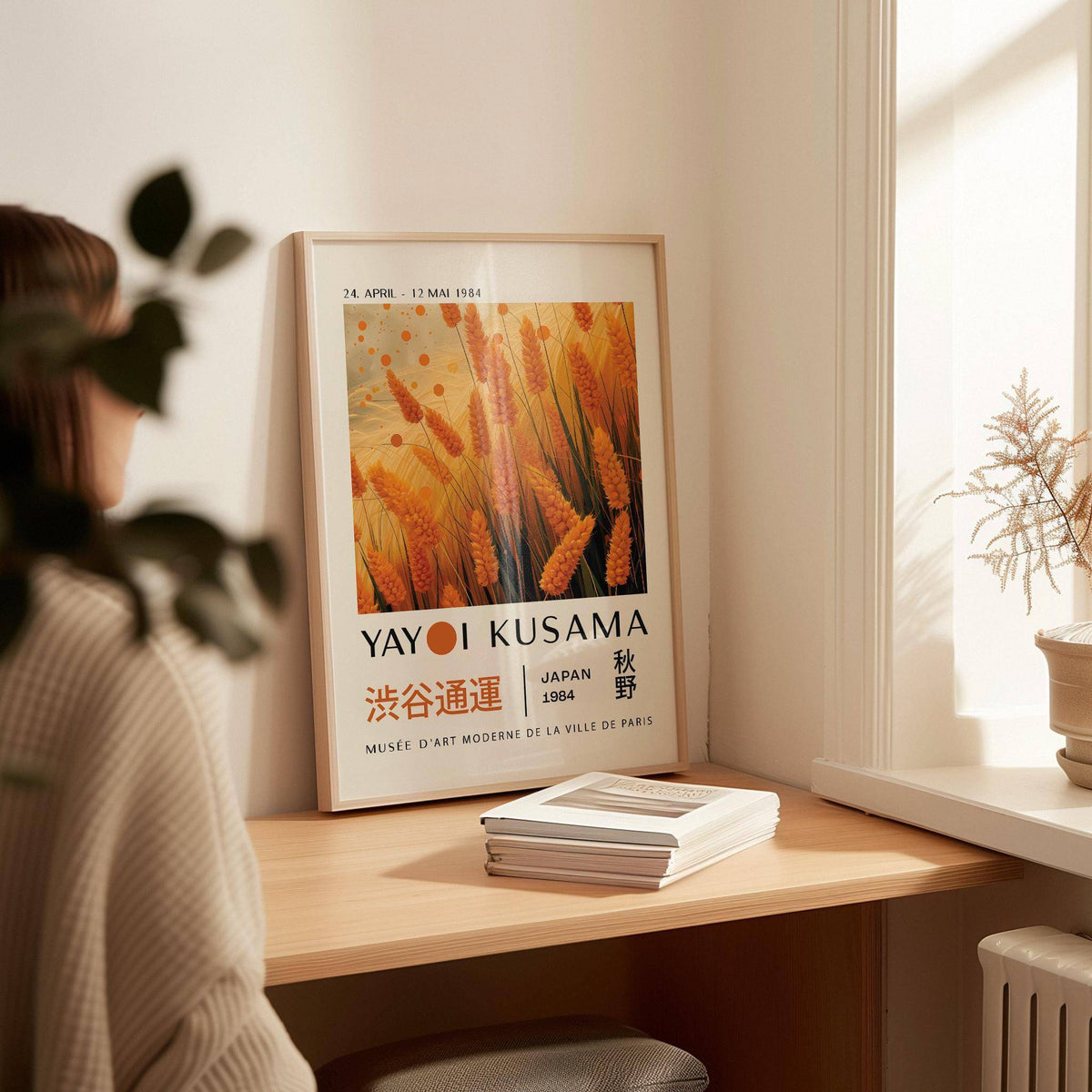 Autumnal wall art leaning on a desk with orange wheat plants and text beside potted plant by window