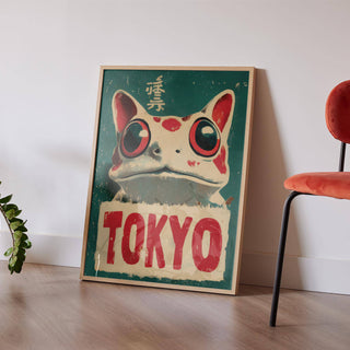Print leaning on a floor with a red chair and a green plant nearby featuring a frog with large eyes and red text