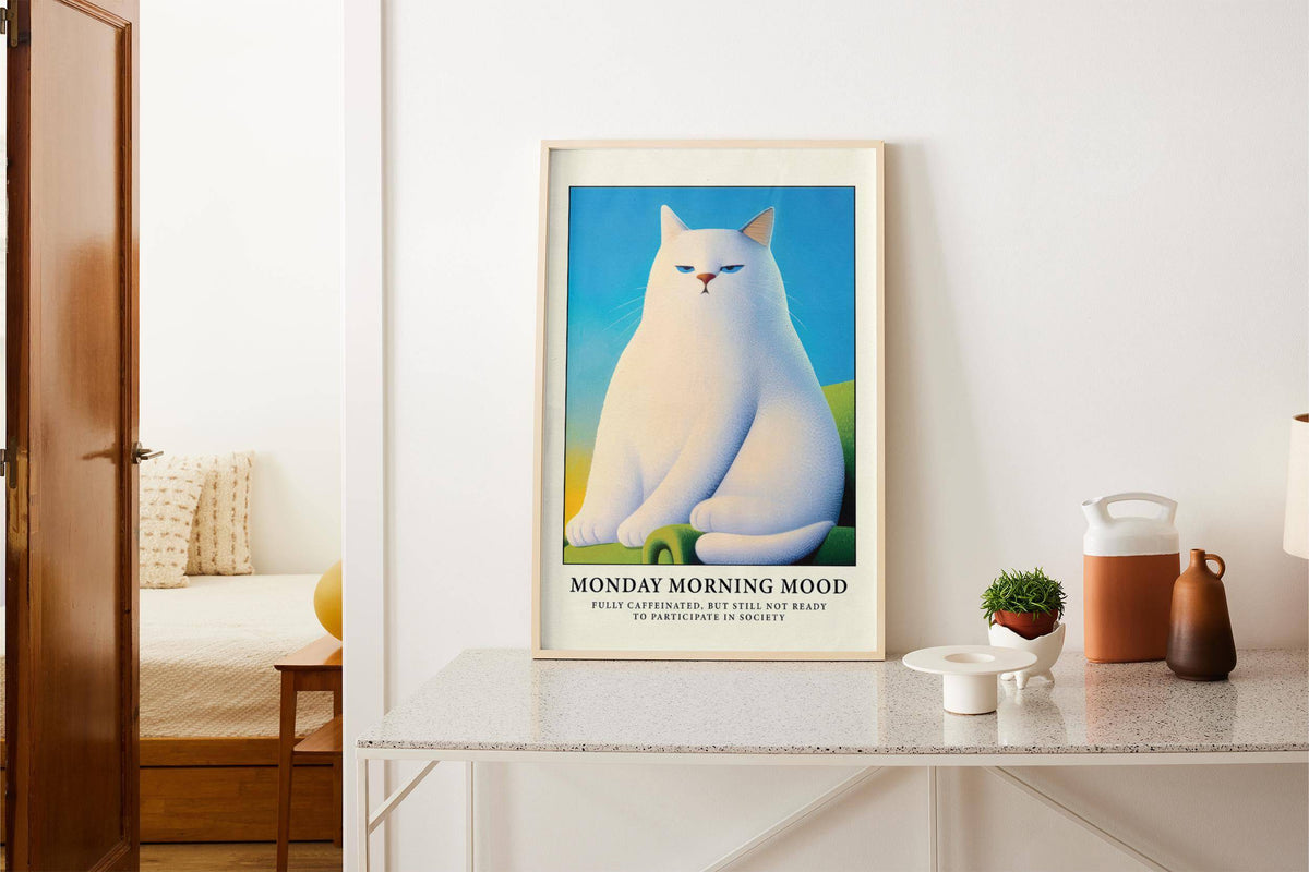 Monday Mood Cat Poster print leaning on a white counter with small plants and a jug nearby