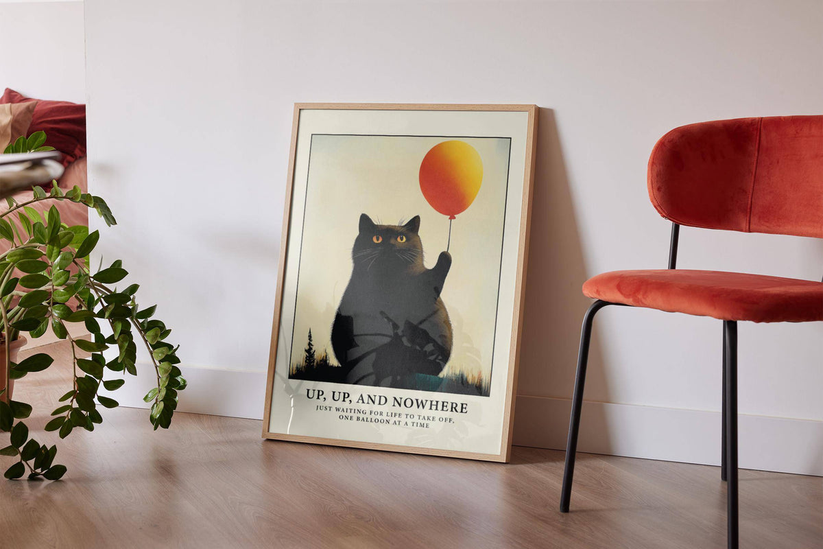 Print leaning on floor of black cat holding orange balloon with text beside a red chair and plant