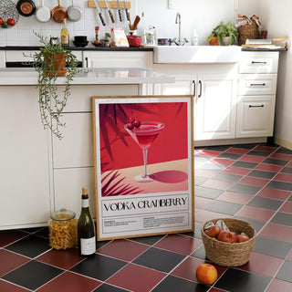 Print leaning on a kitchen floor with black and red tiles and a basket of fruit nearby