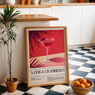 Print leaning on the floor of a kitchen showing a vodka cranberry cocktail illustration with red and pink shades and a potted plant nearby
