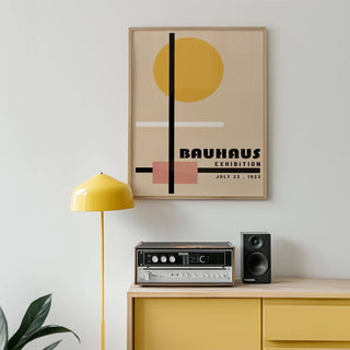 Office prints framed Bauhaus exhibition poster with geometric shapes in beige, black, yellow and pink above a yellow cabinet with audio