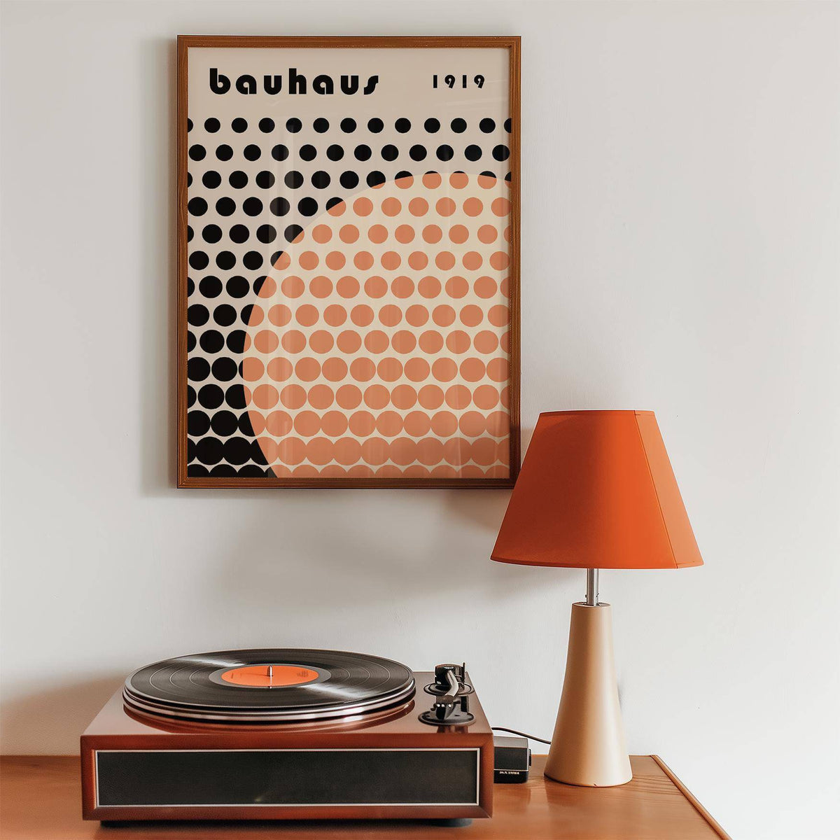 Cool Art Poster framed print on a wall with orange and black dots above a record player and lamp