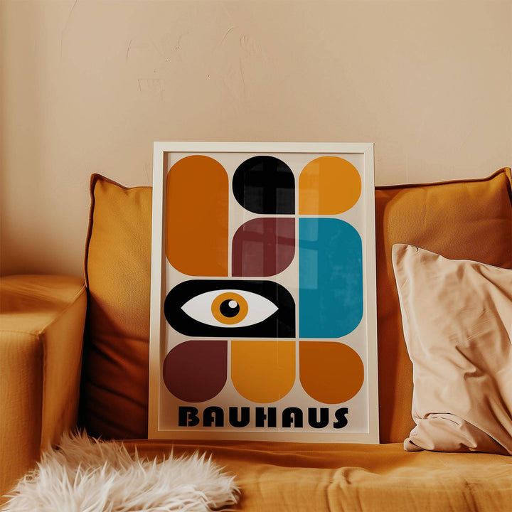 Framed print of geometric shapes wall art with an abstract eye in warm colours on a leather sofa with a cushion