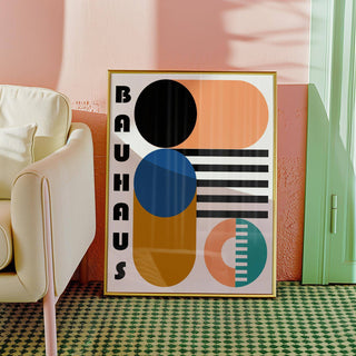 Framed Bauhaus geometric shapes print with blue black and orange shapes leaning against a wall near a cream chair