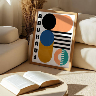 Framed print leaning on a beige carpet with an open book nearby showing abstract geometric shapes in blue and orange