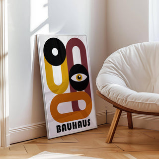 Print leaning with abstract eye and geometric shapes in black, mustard, and rust near a white chair