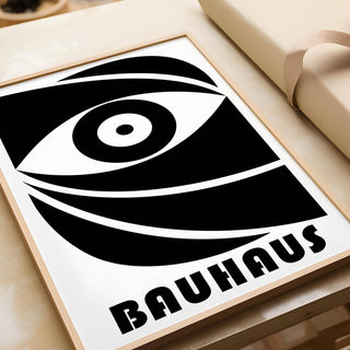 Framed Black Eye Poster with a minimalist abstract eye in black and white leaning on a wooden surface next to wrapping paper