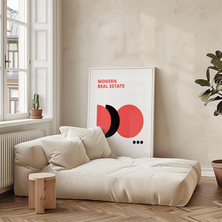 Print leaning on floor with modern real estate text in red black and white beside a cream sofa and small wooden stool