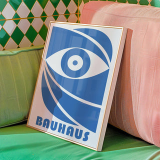 Framed Bauhaus print with a stylised blue eye leaning on cushions with green geometric tiles