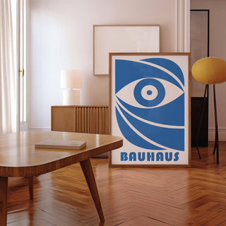 Bauhaus framed print of a stylised blue eye leaning on a wooden sideboard with a white lamp