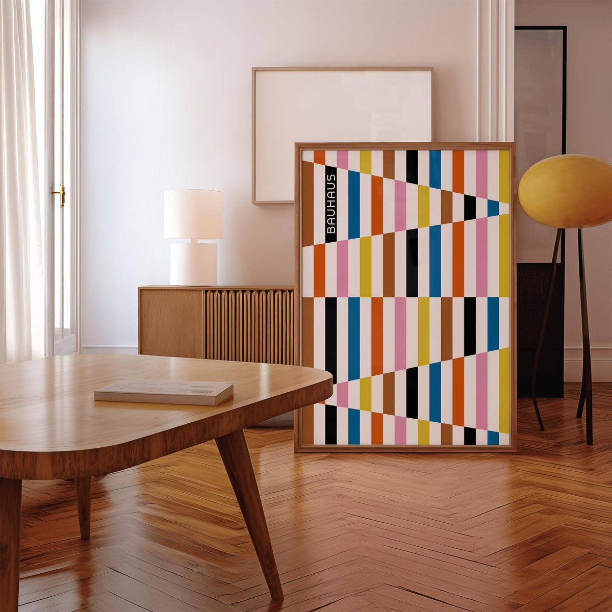 Framed print of colorful geometric blocks with an emphasis on gold and blue leaning against a wall above parquet flooring with yellow lamp