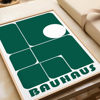 Close-up of green geometric shapes in Bauhaus style framed print leaning on a wooden surface with wrapping paper nearby