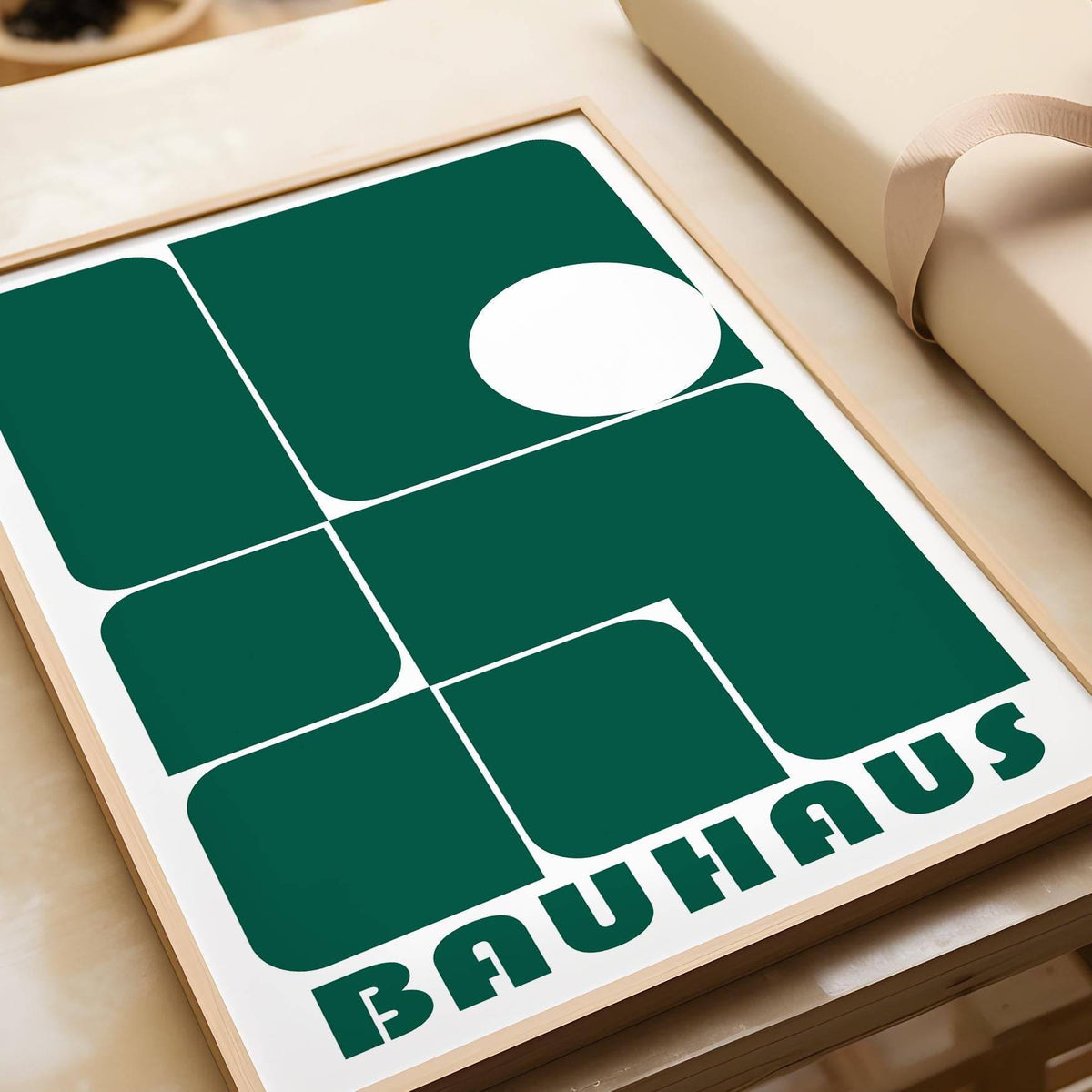Close-up of green geometric shapes in Bauhaus style framed print leaning on a wooden surface with wrapping paper nearby