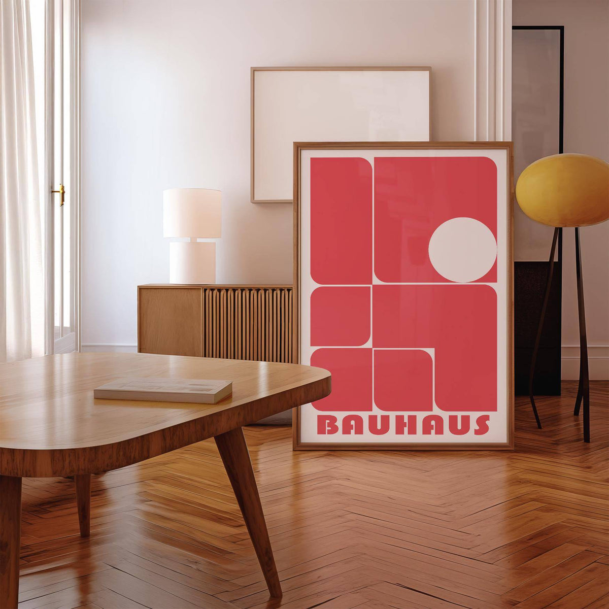 Print leaning on the floor red wall art decor with rounded rectangles and a white circle in a minimalist room with wooden flooring