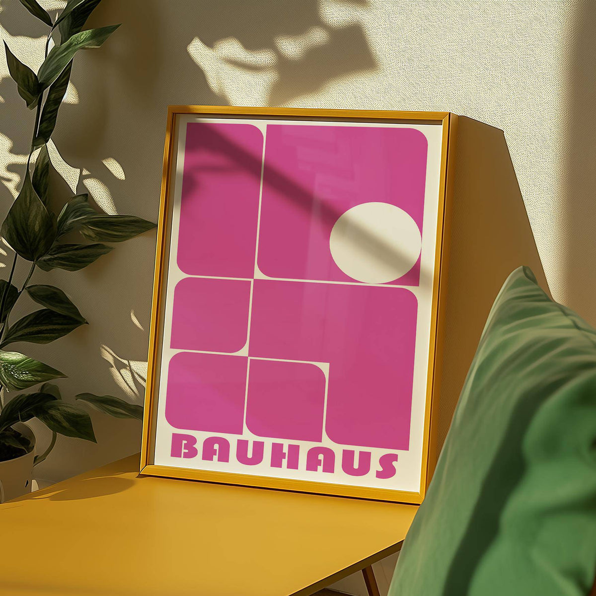 Framed wall art pink with bauhaus geometric shapes on a yellow surface near a green cushion and plant