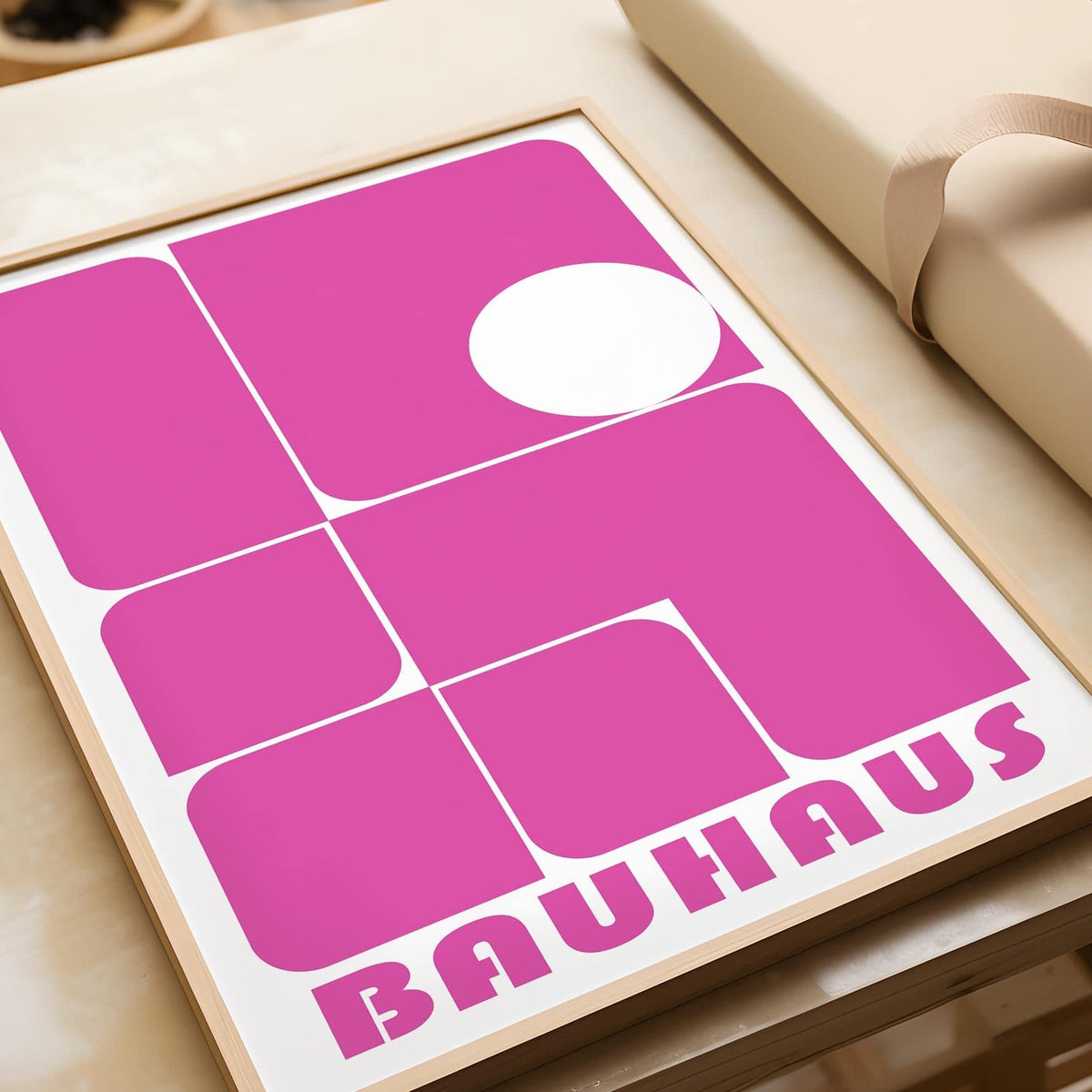 Framed Wall Art Pink with abstract geometric shapes in bold pink and white beside a wrapped gift