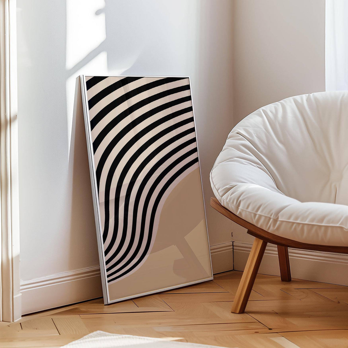 Print leaning on floor showing beige abstract art with curved black and cream stripes beside a white cushioned chair