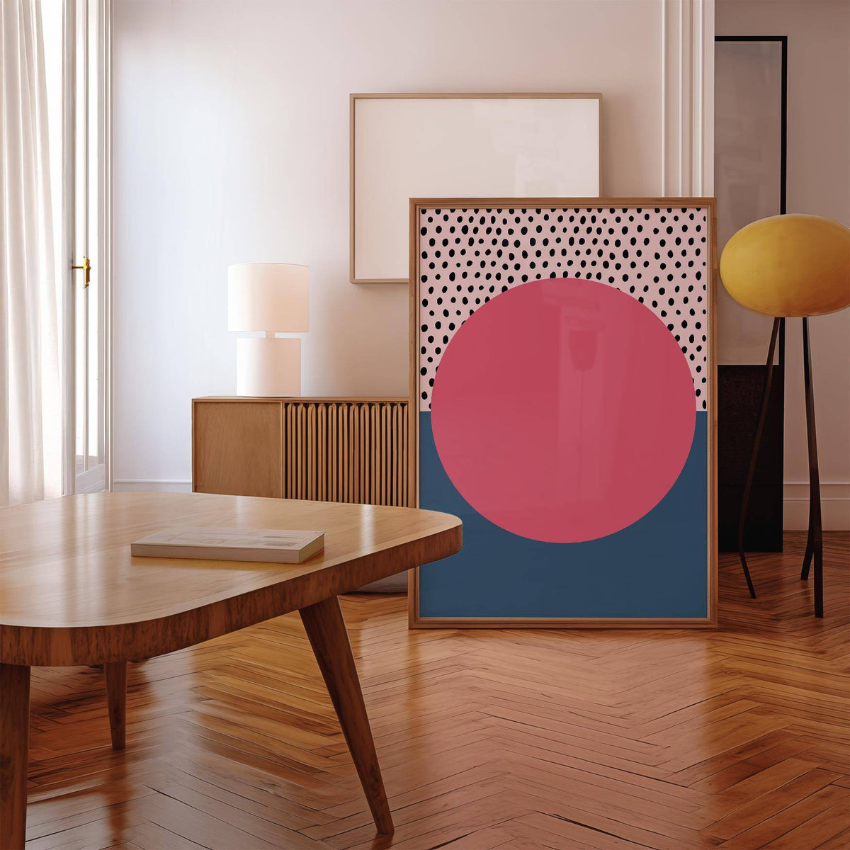 Print leaning on floor of Modern Abstract Art Geometric with pink circle and black dots near a wooden table