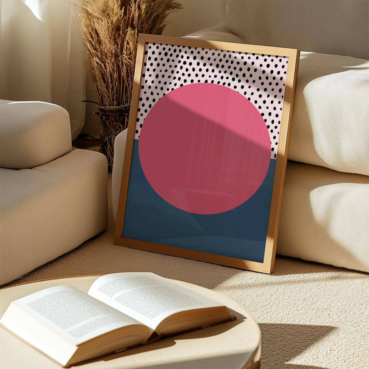Print leaning on a shelf of modern abstract art geometric with pink circle and black dots near an open book