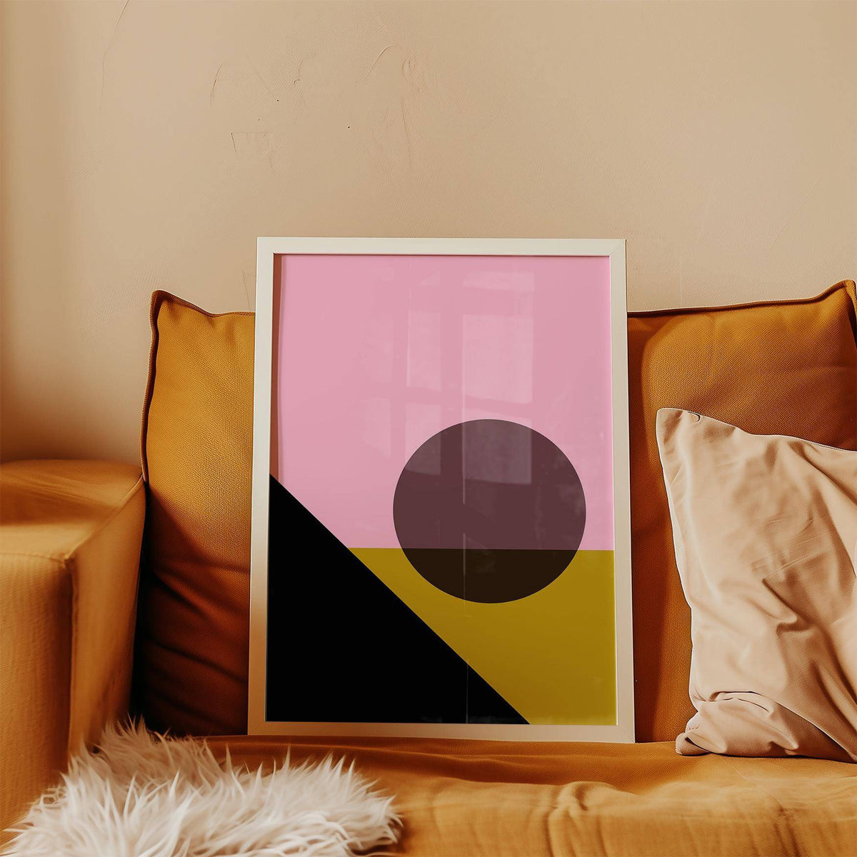 Bright Colored Artwork framed print with pink, black and gold geometric shapes resting on an orange sofa with cushions