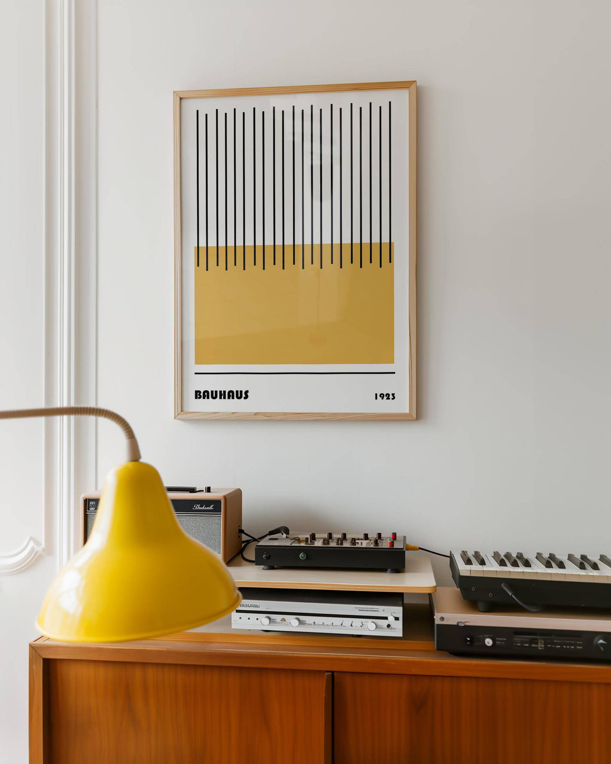 Modern Geometric Art framed print with yellow block and black lines above a wooden cabinet with audio equipment and yellow lamp