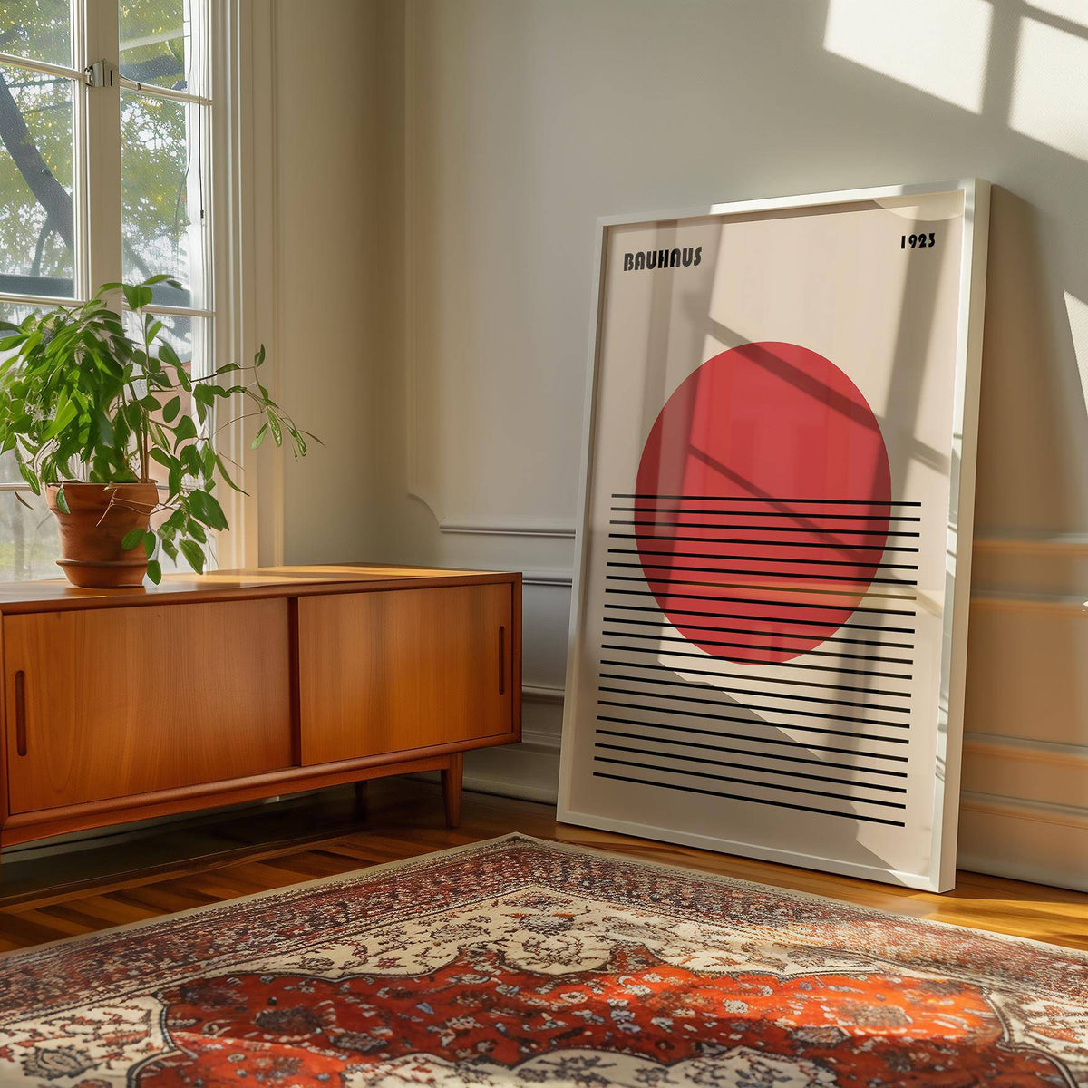 Framed Geometric Art Print featuring a red orb with black lines leaning next to a wooden sideboard and plant in a sunlit room