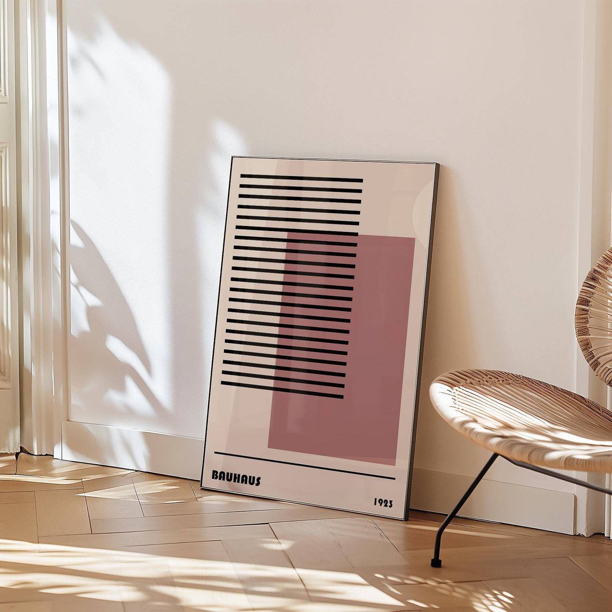 Print leaning against a wall with Bauhaus 1923 Art showing black lines and a pink square beside a wicker chair