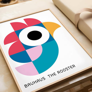 Framed geometric pattern art of an abstract rooster in red, blue and yellow on a table with wrapping paper
