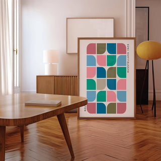 Print leaning on floor with geometric blocks in pink blue and green tones near wooden table in living room