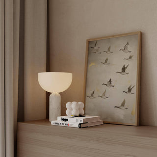 Print leaning on a shelf of flying geese in soft greys and beige with a lamp nearby