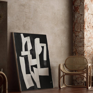Wabi Sabi wall art with white abstract shapes on black leaning on a floor next to a cane chair
