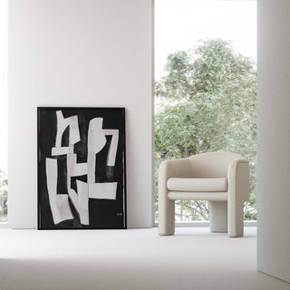 Print leaning on the floor with white abstract shapes on black beside a cream armchair and window