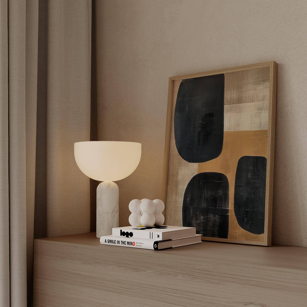 Earthy wall art leaning on a wooden shelf with beige and black abstract shapes and a white lamp