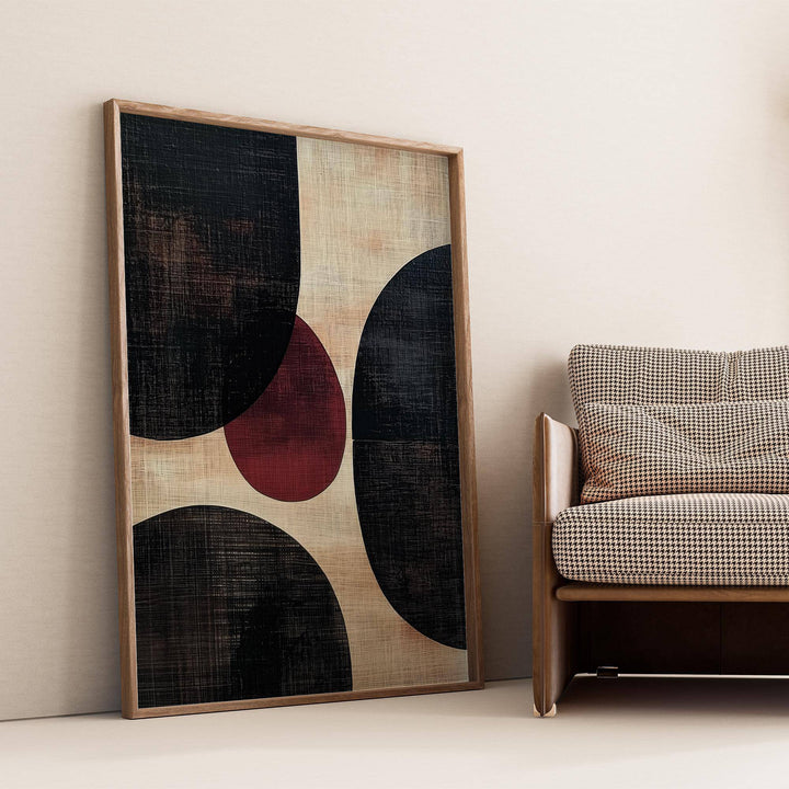 Wall Art Abstract leaning print with abstract rounded shapes in black and red beside a patterned sofa
