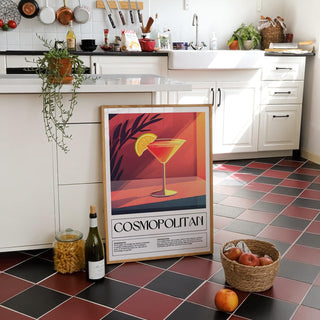 Drink poster art leaning on a tiled floor with a bottle and basket nearby in a kitchen