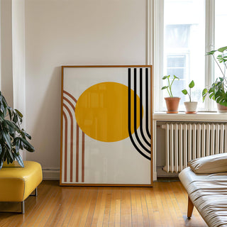Print leaning on wooden floor of an orange sun circle with black and brown curved stripes next to plants