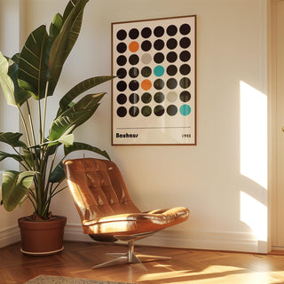 Graphic prints hanging on a wall above a brown leather chair with a plant nearby in natural light
