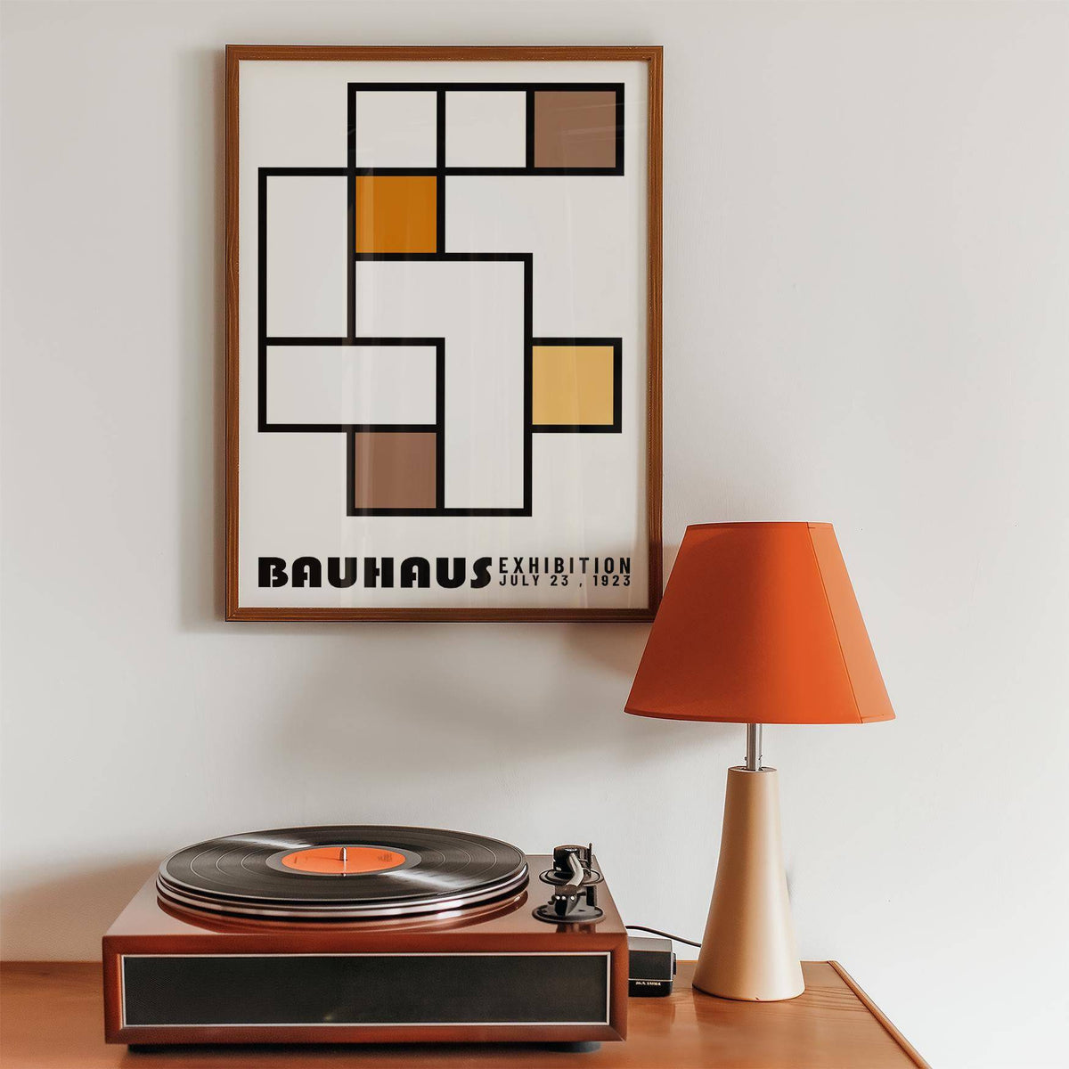 Framed print of geometric abstract art with orange and brown blocks above a record player and orange lamp