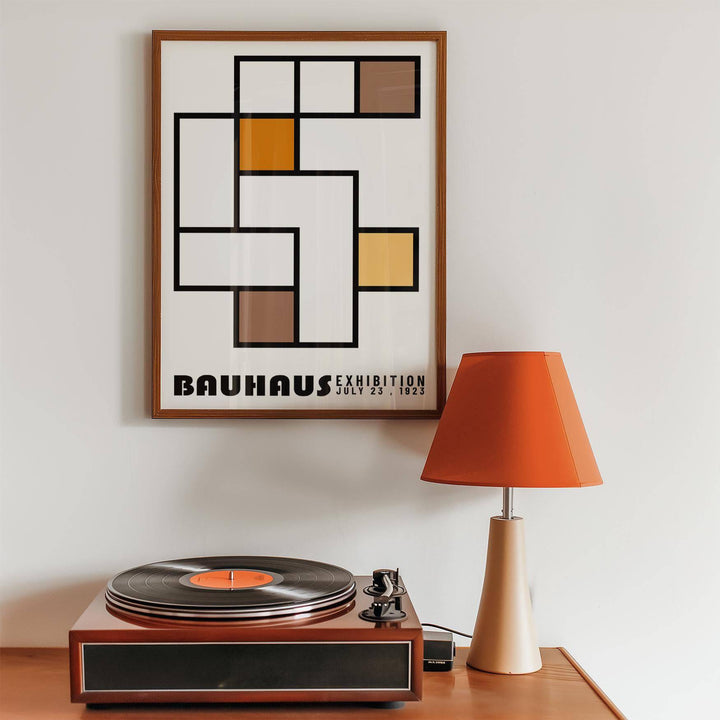 Framed print of geometric abstract art with orange and brown blocks above a record player and orange lamp