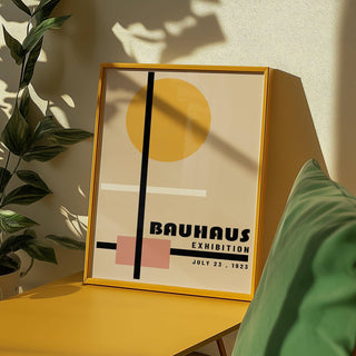 Framed print of abstract geometric shapes with a yellow circle and pink square leaning on a yellow surface near a green plant