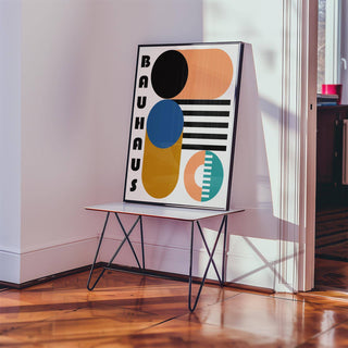 Print leaning on a table with Bauhaus geometric shapes in black, blue, orange and teal in a bright room