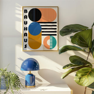 Bauhaus geometric shapes print on a wall with orange and blue shapes above a white table with blue lamp and green plant