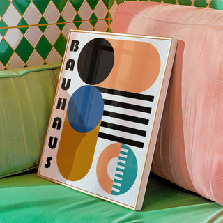 Framed Bauhaus Geometric Shapes print leaning on a green cushion next to a pink cushion