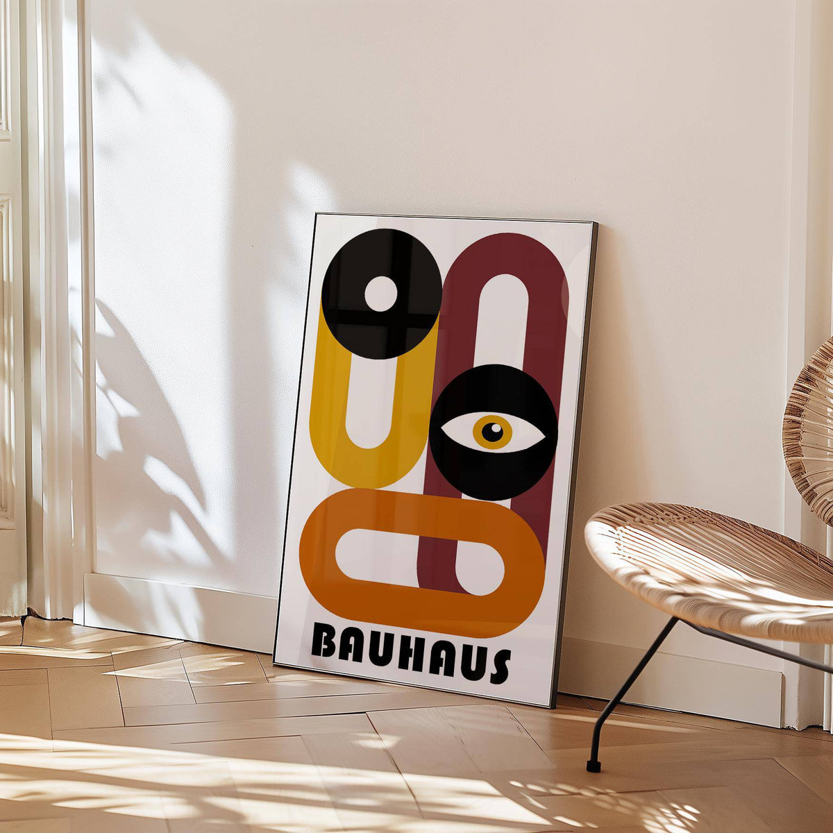 Print leaning on a floor with retro home decor abstract eye design in black, ochre and rust beside a rattan chair