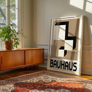 Geometric wall hanging leaning on the floor beside a wooden sideboard with a green plant in sunlight