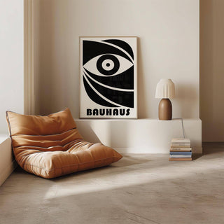Black Eye Poster leaning on white shelf with an abstract black and white eye and text Bauhaus beside a brown vase lamp and stack of books