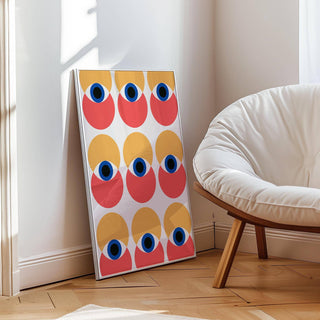 Print leaning on floor showing abstract eyes in yellow and red near a white cushioned chair